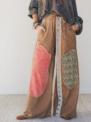 Brown wide-leg pants with colorful patches worn by a person against a white background