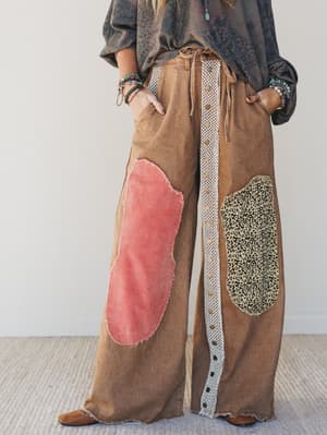 Brown wide-leg pants with colorful patches worn by a person against a white background