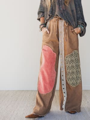 Person wearing a brown patchwork pants with pink and leopard print sections on a plain background