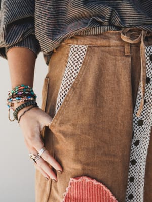 Person wearing a brown apron with decorative elements, holding their hand out.