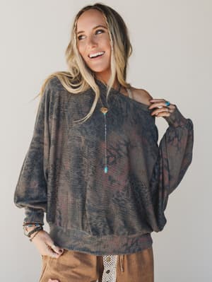 Woman wearing a patterned sweater and brown pants against a plain background