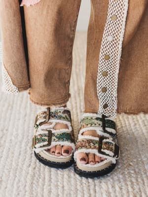 Decorative sandals worn with brown pants on a textured surface