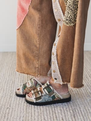 Person wearing patterned sandals with brown pants on a neutral background