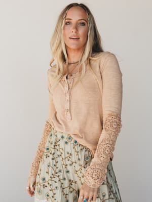 Woman wearing a beige long-sleeve top with lace cuffs and a floral skirt on a plain background