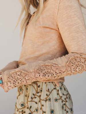 Close-up of a person wearing a peach blouse with lace cuffs and a patterned skirt.