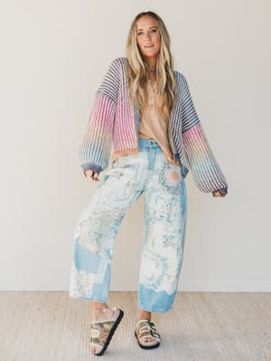 Woman wearing a colorful striped cardigan, beige top, and floral pants indoors.
