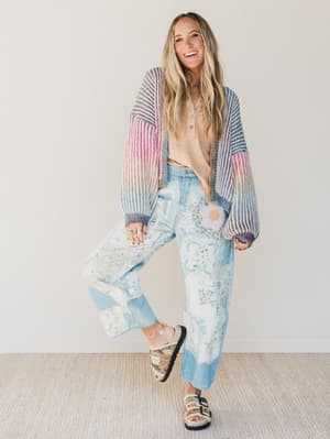 Woman wearing a colorful striped cardigan and patterned pants against a white background