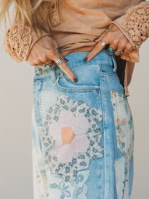 Person wearing a patchwork denim skirt with floral patterns and a beige top.
