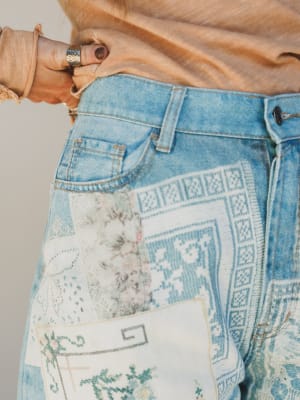 Close-up of a person wearing a denim jacket with intricate embroidery on the back pocket.