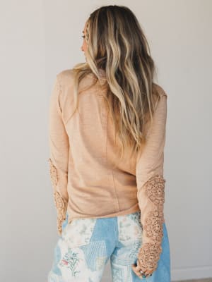 Woman wearing a beige top with lace sleeves against a plain background