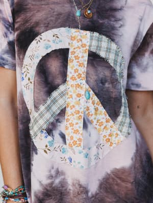 Floral peace sign design on a tie-dye shirt with visible tattoos.