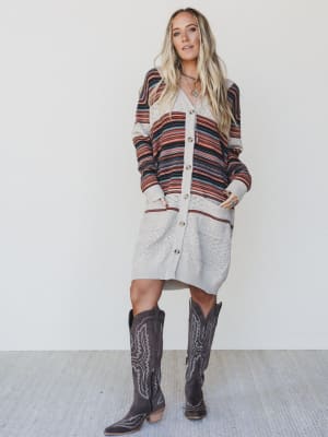 Woman wearing a striped cardigan and gray dress with cowboy boots on a white background