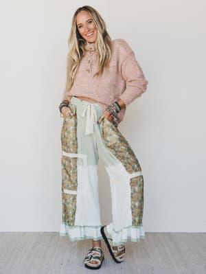 Woman wearing a pink sweater and floral pants with a sheer overlay against a white background