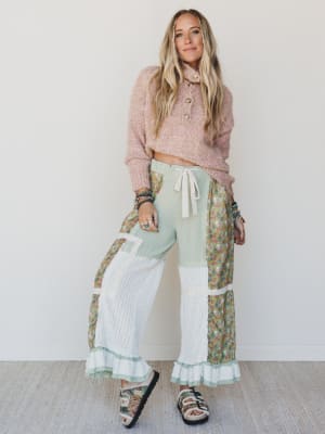 Woman wearing a pink sweater and patchwork pants against a white background