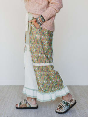 Person wearing a floral skirt, pink sweater, and sandals on a plain background