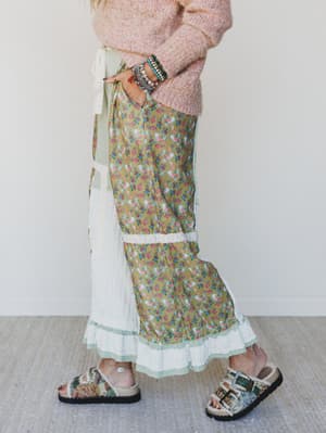 Person wearing a floral skirt, pink sweater, and sandals on a plain background