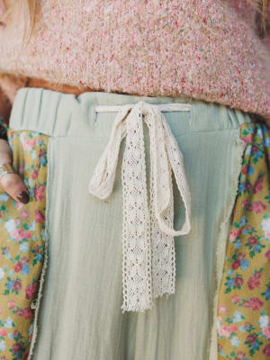 Person wearing a light green pants with a lace ribbon and floral top.