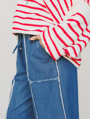 Person wearing a red and white striped sweater and blue jeans on a plain background