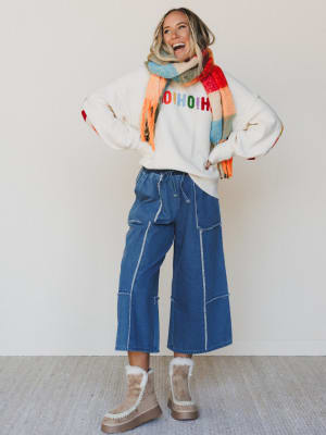 Person wearing a colorful sweater, scarf, blue jeans, and brown boots on a plain background