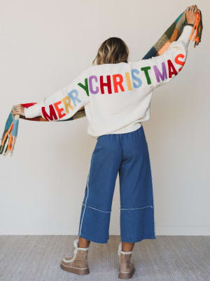 Person wearing a sweater with 'Merry Christmas' in colorful letters, standing against a plain background.