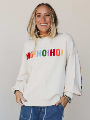 Woman wearing a white sweater with colorful 'HO HO HO' text on a plain background