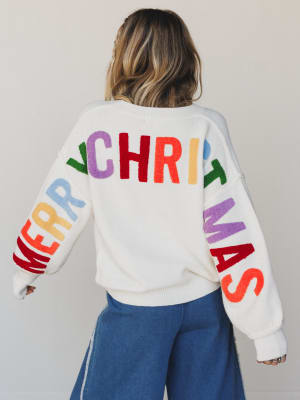 Person wearing a white sweater with 'Merry Christmas' in colorful letters on a plain background