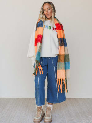 Person wearing a colorful scarf, white shirt with text, blue jeans, and beige boots on a plain background