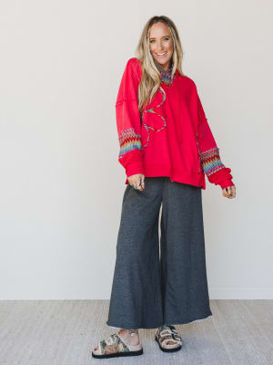 Woman wearing a red embroidered top and wide-leg gray pants against a white background