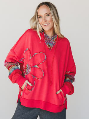 Woman wearing a red hoodie with a colorful flower design on a plain background