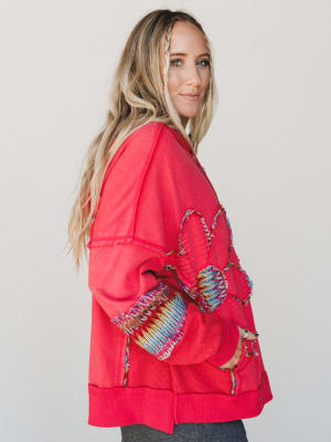 Woman wearing a red top with colorful patterns on a plain background