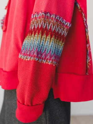 Close-up of a red garment with colorful patterned cuffs and hem.