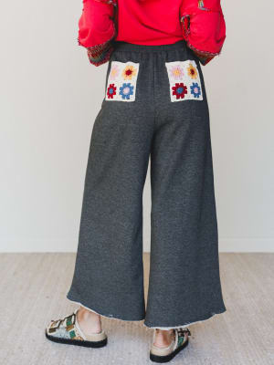 Person wearing gray wide-leg pants with floral patch pockets against a plain background