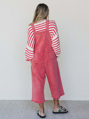 Person wearing a red striped shirt and pink overalls standing against a white wall.