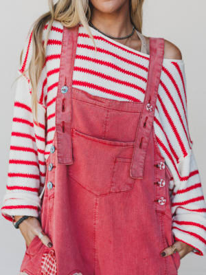 Person wearing a red and white striped sweater with a pink denim overall dress against a plain background