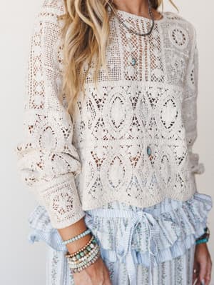 A cream crochet top with intricate medallion paneling is layered over a soft blue floral and stripe ruffle skirt — the kind of outfit that looks like it came together effortlessly but definitely did not.