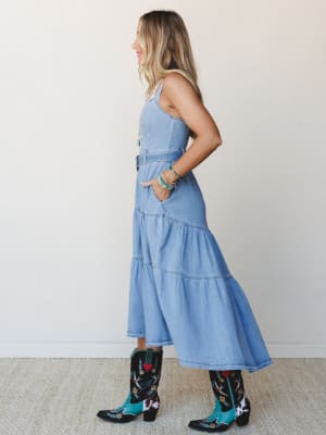 A tiered denim midi dress in a soft cloud wash blue, styled with embroidered western cowboy boots and turquoise stacked bracelets — the kind of outfit that feels equally at home at a summer concert or a weekend farmers market.