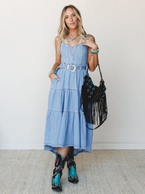 A sun-washed denim midi dress styled with embroidered cowboy boots, a fringe crossbody bag, and layered turquoise jewelry — the kind of outfit that makes a country concert feel like a whole personality.