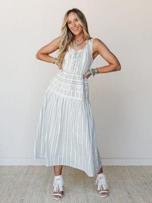 A striped midi dress in cream and sage olive gets styled with white fringe heels and stacked turquoise jewelry — the kind of outfit that works just as hard at a summer wedding as it does wandering a farmers market.