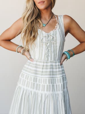 A tiered striped midi dress in cream and olive gets the full boho treatment — lace-up bodice, eyelet trim, and a stack of turquoise bracelets that feel completely at home here.