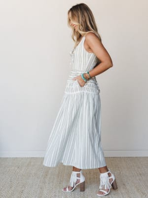 A sun-warmed midi dress in soft olive and cream stripes styled with white fringe heels and turquoise stacked bracelets — the kind of outfit that feels equally at home at a farmers market or a summer wedding.
