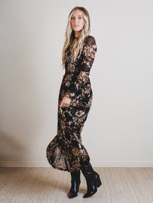 Woman wearing a black floral dress standing against a plain background