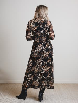 Woman wearing a long floral dress with sheer sleeves against a plain background