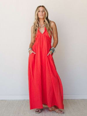 A flowy cherry red halter maxi dress in crinkle gauze fabric, styled with stacked turquoise and beaded bracelets and flat sandals — effortless and a little bold, like she packed one dress and it was the right call.