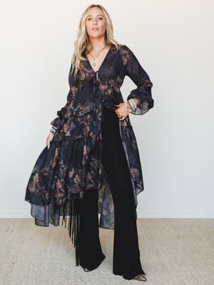 A flowy, dark floral duster with tiered ruffles and fringe hem layered over wide-leg black pants — moody, expressive, and styled like someone who knows exactly how to walk into a room.