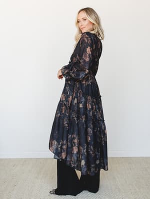 A flowy dark floral duster layered over wide-leg black pants, shot in soft studio light — the kind of outfit that feels equally at home at a dinner reservation or a Sunday farmers market.