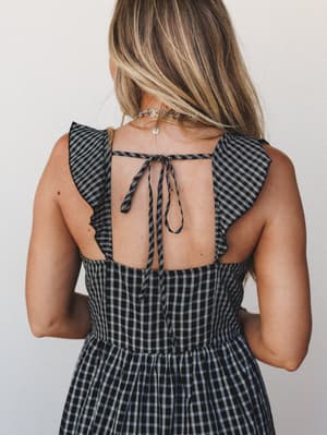 A close back-detail shot of a black plaid dress with flutter sleeves and an open tie-back, showing the kind of thoughtful design detail you notice — and then can't stop noticing.