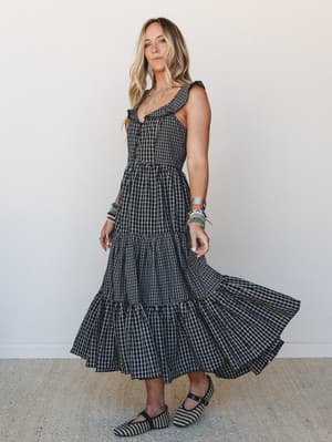 A tiered gingham midi dress in black and white swirls mid-motion against a clean studio wall — the kind of dress that makes you want to spin in a field or show up to a fall farmers market looking like you planned it effortlessly.