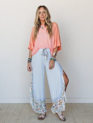 A breezy two-piece set styled with stacked boho jewelry and flat sandals — the wide-leg floral-trim pants and relaxed coral top feel like a summer afternoon that has nowhere to be.