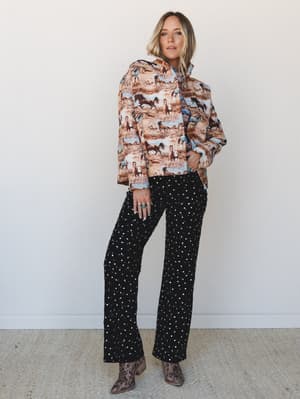 A full-body model shot layered with personality — a horse-print puffer jacket over a coordinating top, paired with black wide-leg sequin pants and leopard ankle boots, shot against a clean white studio wall.