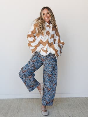 A smiling model in a chunky crochet sweater and wide-leg butterfly-print pants — the kind of outfit that feels like a good mood made wearable.